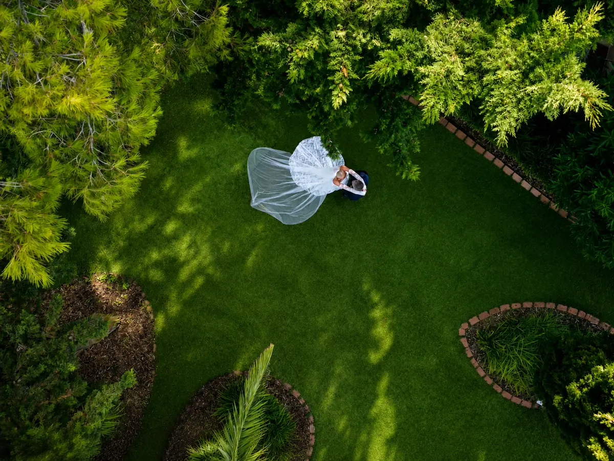 Novia con el velo extendido sobre el césped de un jardín, vista desde arriba