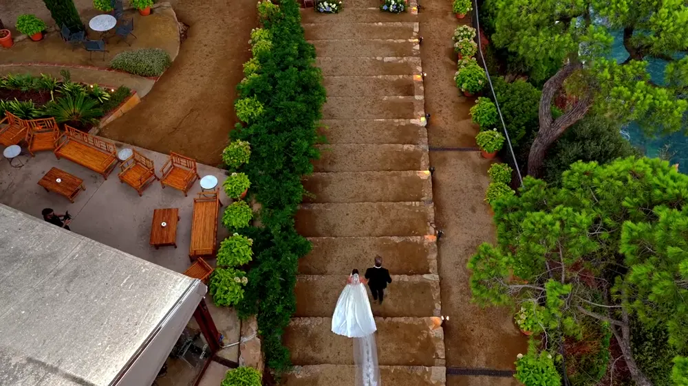 Novios bajando una escalera hacia una ceremonia junto al mar, vista desde un dron