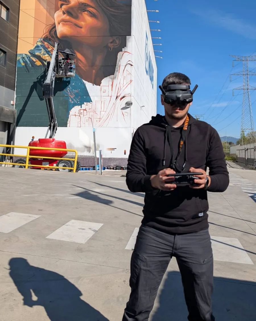 Piloto de drones con gafas FPV y mando delante de un edificio con un mural